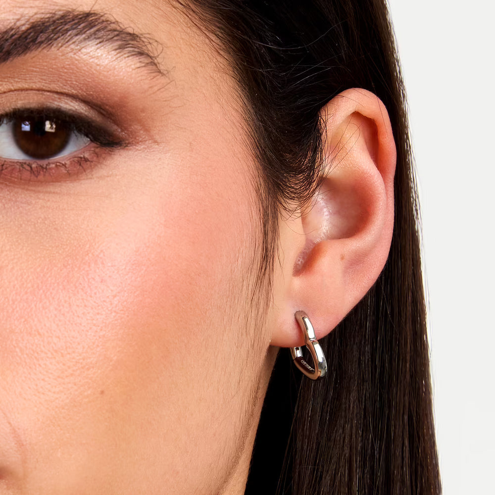 Близък план на ухото с обеца крийол „сърце“ от неръждаема стомана, сребриста.