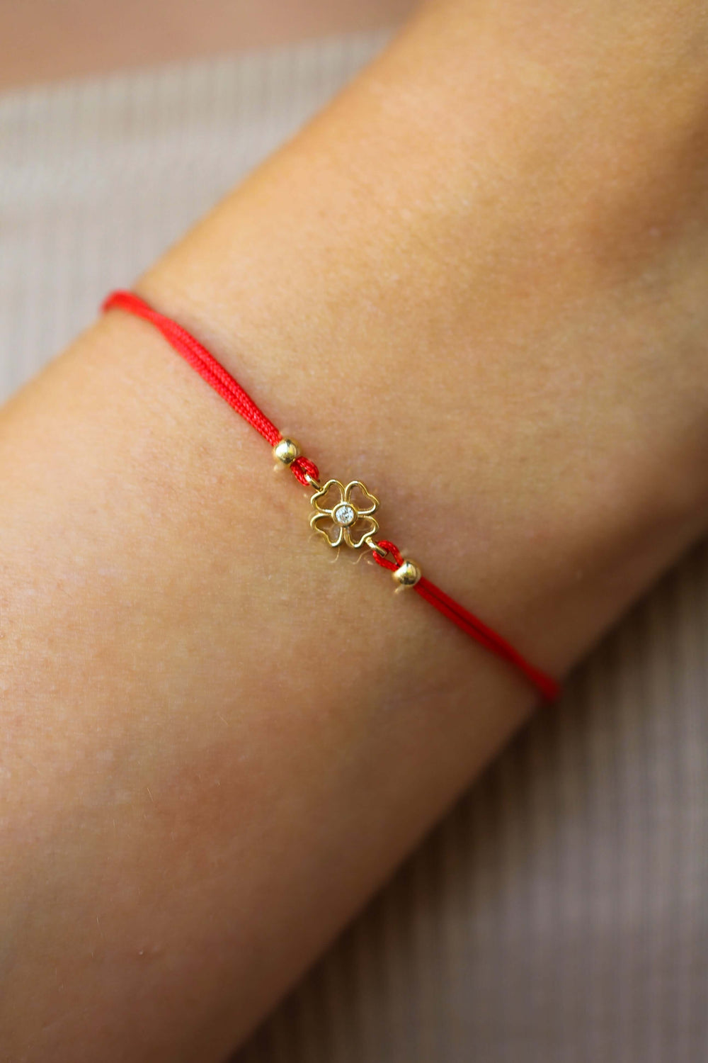 Гривна с червен конец против уроки и четирилистна детелина от 14k злато, представена върху ръка