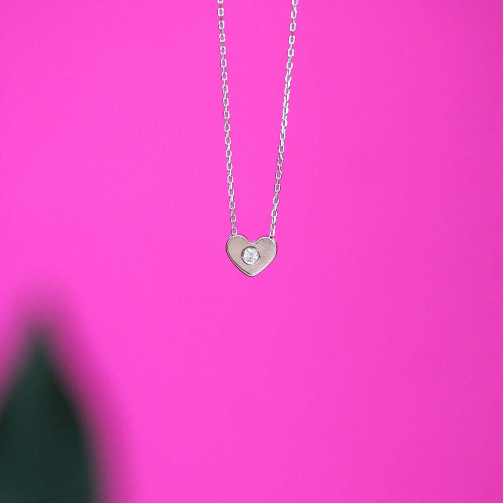 Колие във формата на сърце от бяло злато и диамант заснето на розов фон